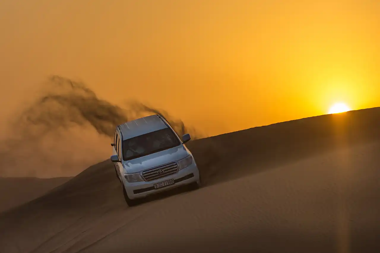 SUV dune bashing on sand dunes during sunrise on a morning desert safari in Dubai