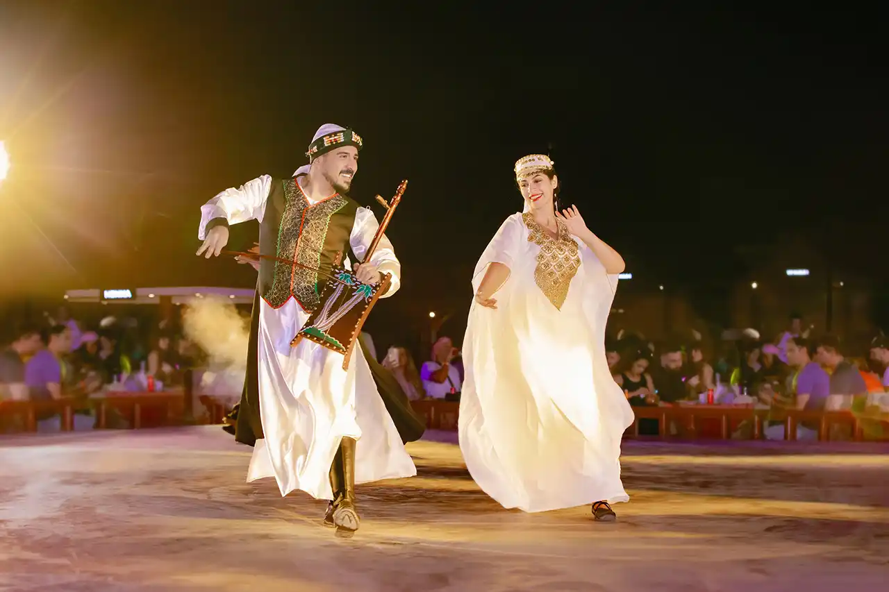 Arabian couple performing in traditional dance at a desert safari in Dubai, holding musical instruments during a cultural show