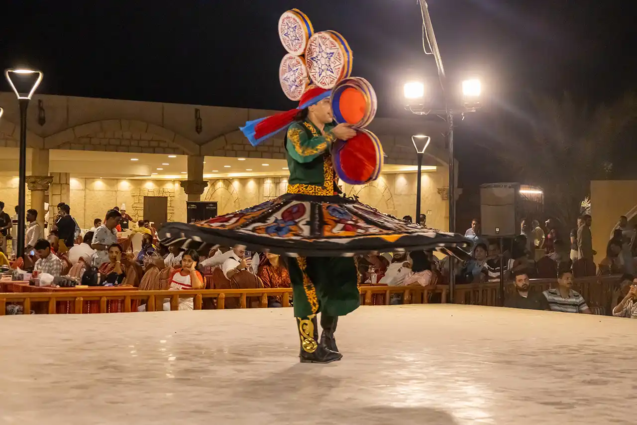 Tanoura dancer performing at a desert safari in Dubai while spinning with colorful skirts and playing hand drums