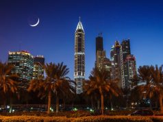 Night View of Dubai with huge skyscrapers and a half moon seen in the sky.