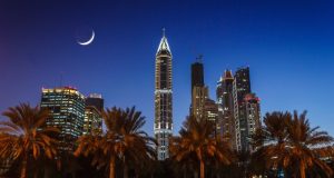 Night View of Dubai with huge skyscrapers and a half moon seen in the sky.